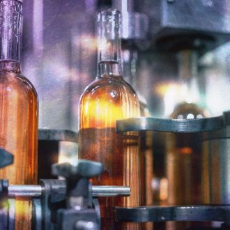Transparent glass bottles filled with wine are arranged in a row on the packaging line to be closed with wooden stoppers